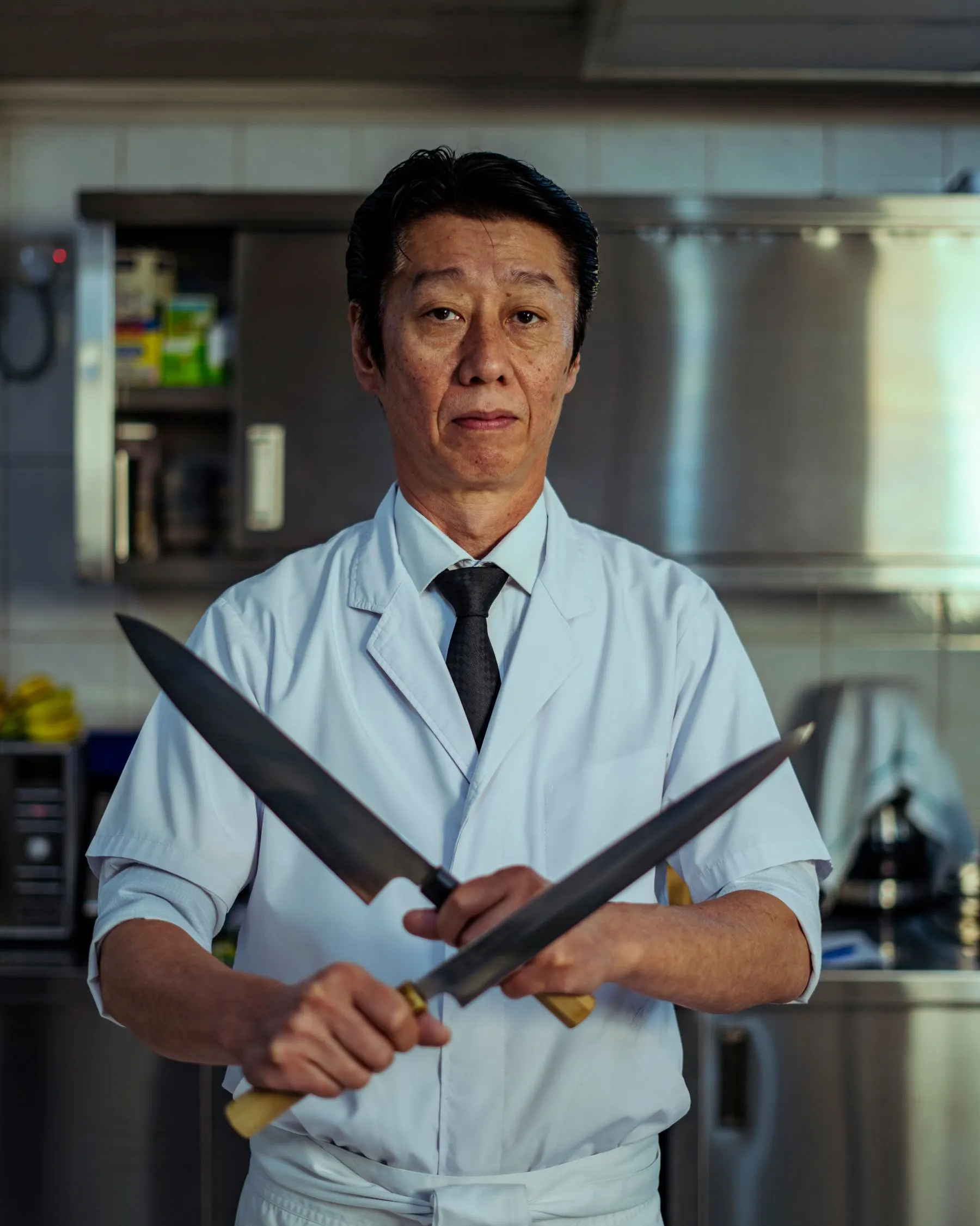 Chef Hiroshi Tanaka holding two knives in a professional kitchen